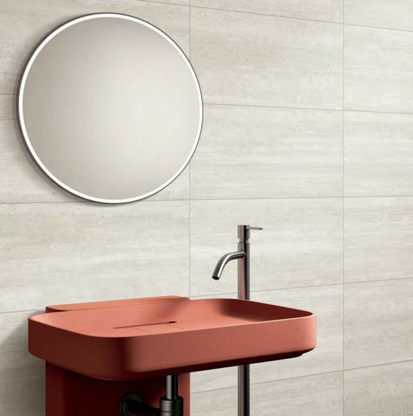 Norcia Vein Cut Light 600x600mm large format light grey wall tiles installed behind a terracotta red pedestal basin with round backlit mirror.