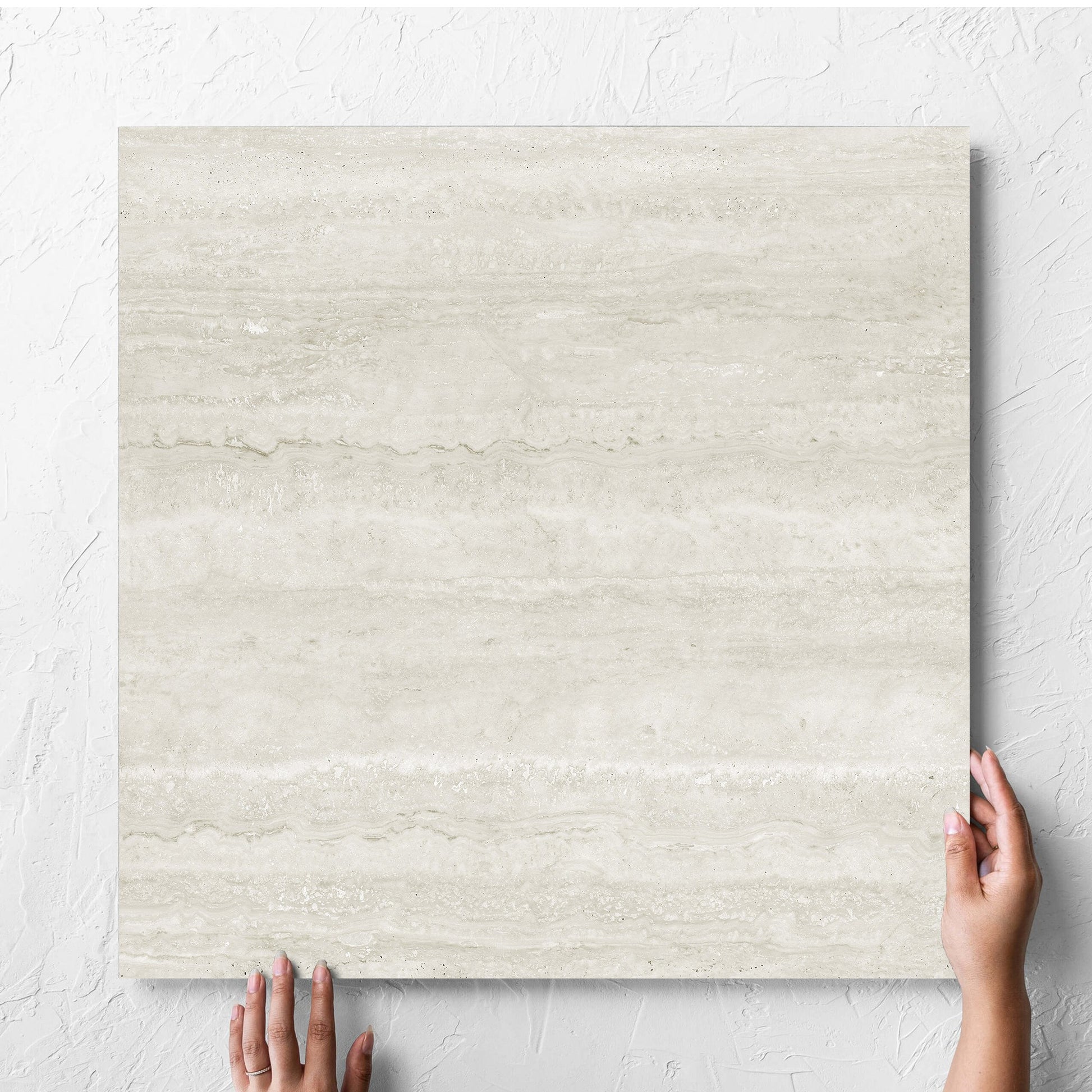 Hand holding a single Norcia Vein Cut Light 600x600mm tile against a white rendered wall, showing the light grey matt surface