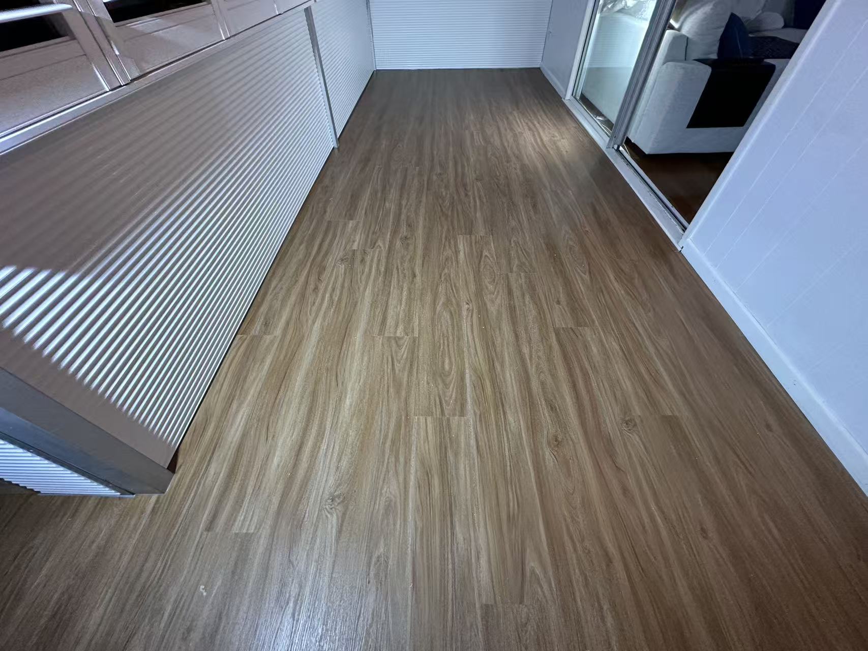 NSW Spotted Gum Elegant SPC Hybrid 6.5mm Flooring 5+1.5mm installed in a narrow balcony hallway with warm brown wood-look planks, white walls, and sliding glass door.