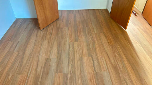 NSW Spotted Gum Elegant SPC Hybrid 6.5mm Flooring 5+1.5mm installed in an empty bedroom showing warm brown wood-look planks with natural grain detail and white skirting boards.