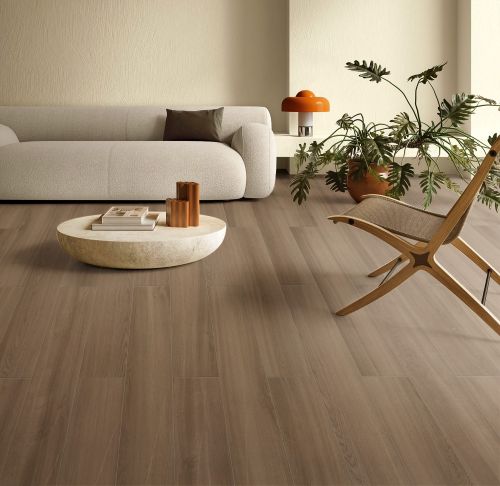 Oakland Oak 200x1200mm wood-effect floor tiles in a warm taupe finish, styled in a modern living room with a bouclé sofa and indoor plants.