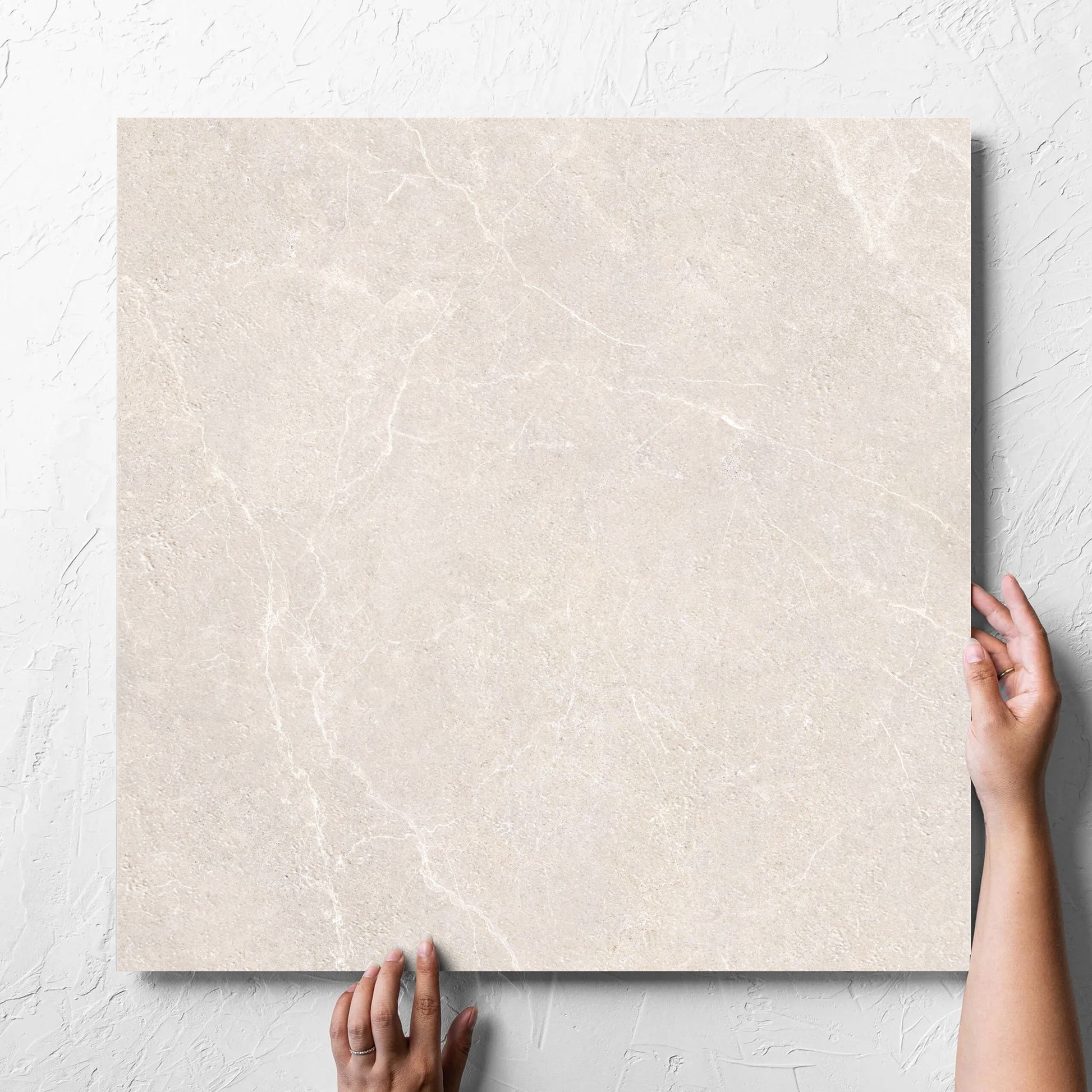 Hand holding a single Oglio Beige 600x600mm tile against a white rendered wall, showing the beige in out non slip surface