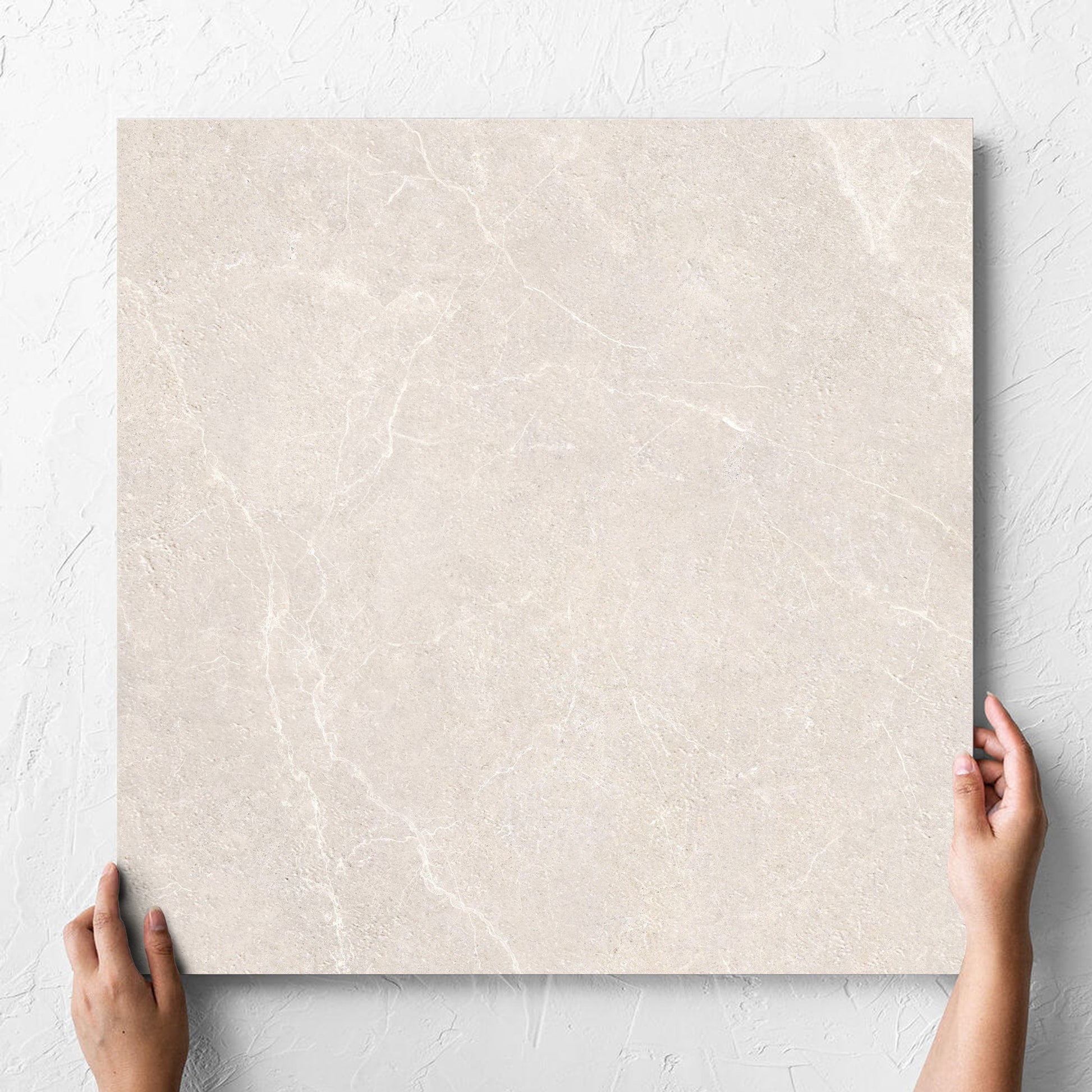 Hand holding a single Oglio Beige Lappato 600x600mm tile against a white rendered wall, showing the lappato surface