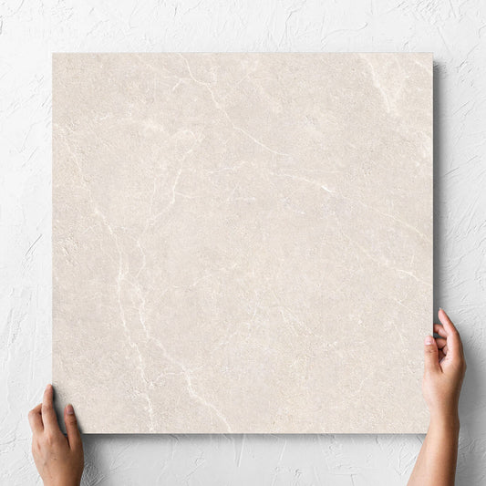 Hand holding a single Oglio Beige Lappato 600x600mm tile against a white rendered wall, showing the lappato surface