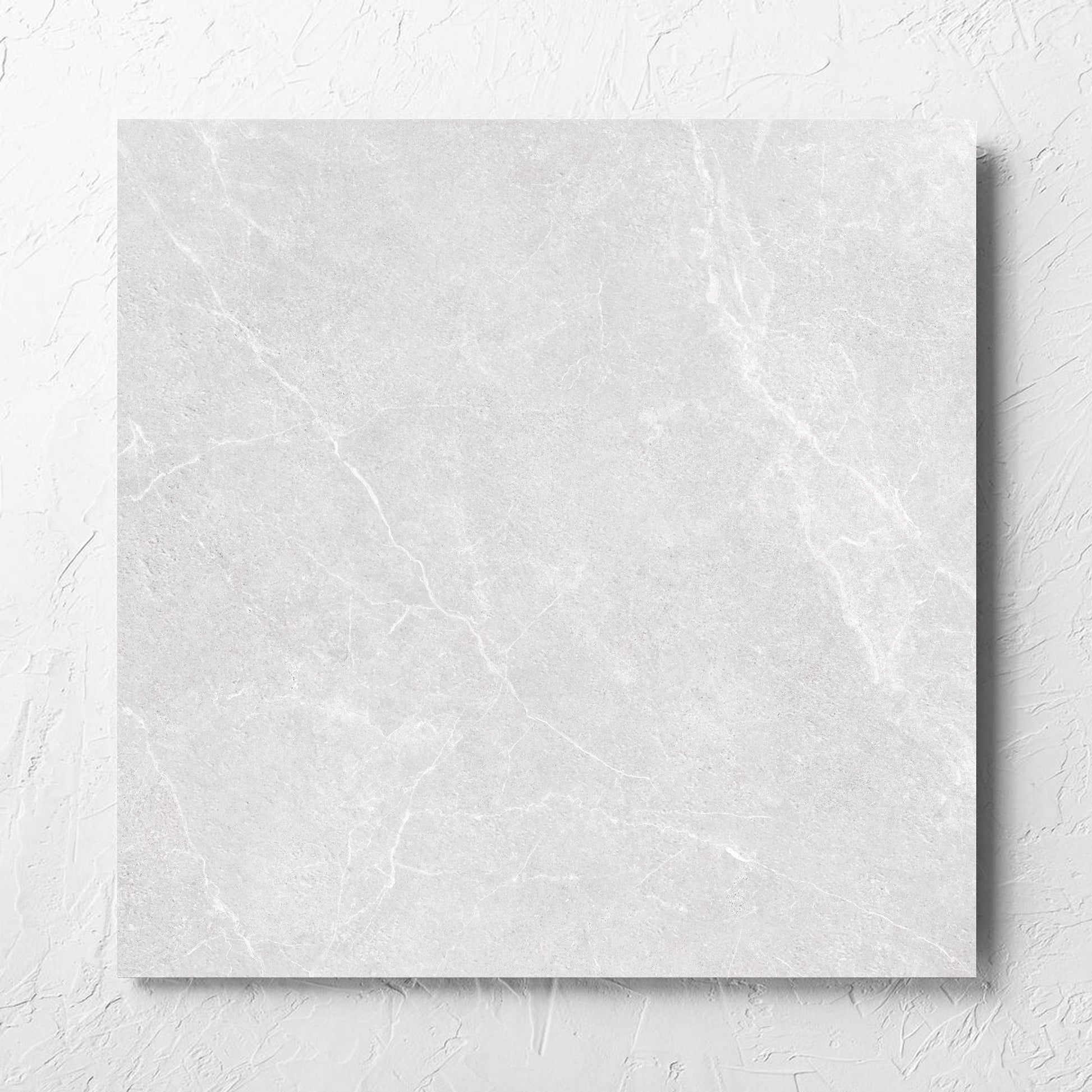 Oglio Silver 600x600mm tile laid flat on a white rendered wall, showing the silver surface