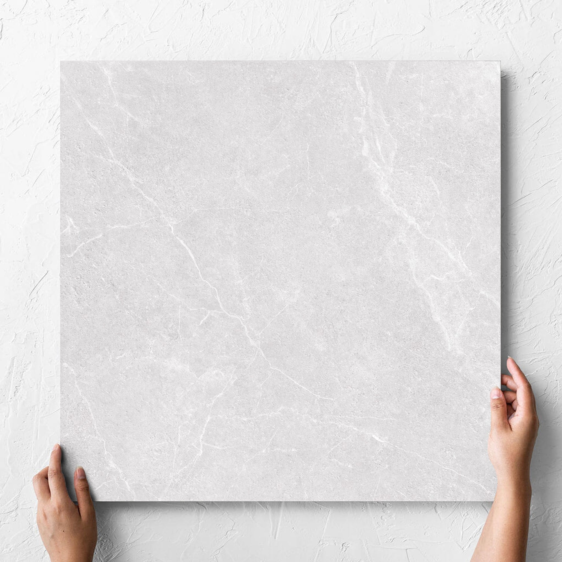 Hand holding a single Oglio Silver Lappato 600x600mm tile against a white rendered wall, showing the lappato surface