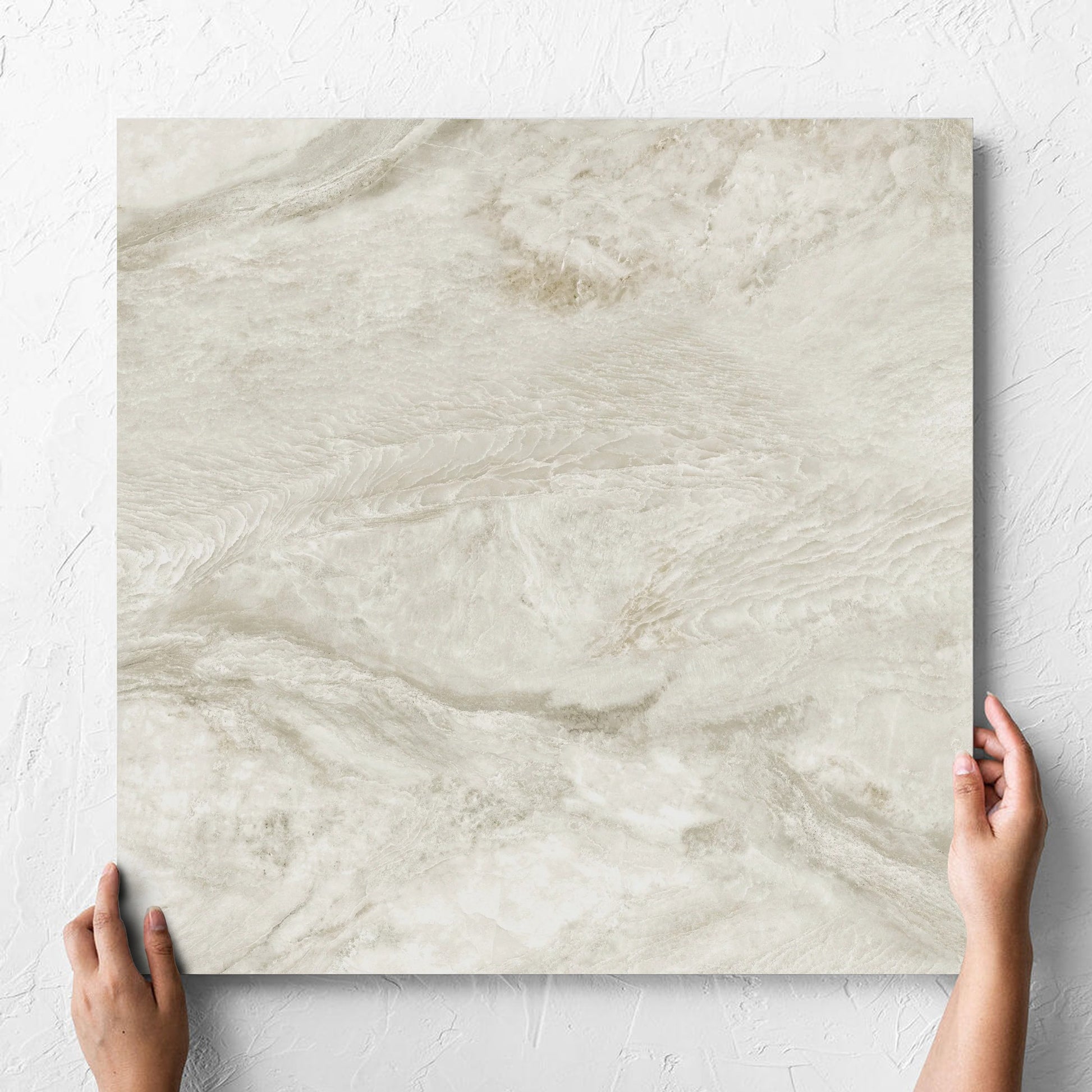 Hand holding a single Onyx Beige Polished 600x600mm tile against a white rendered wall, showing the matt surface