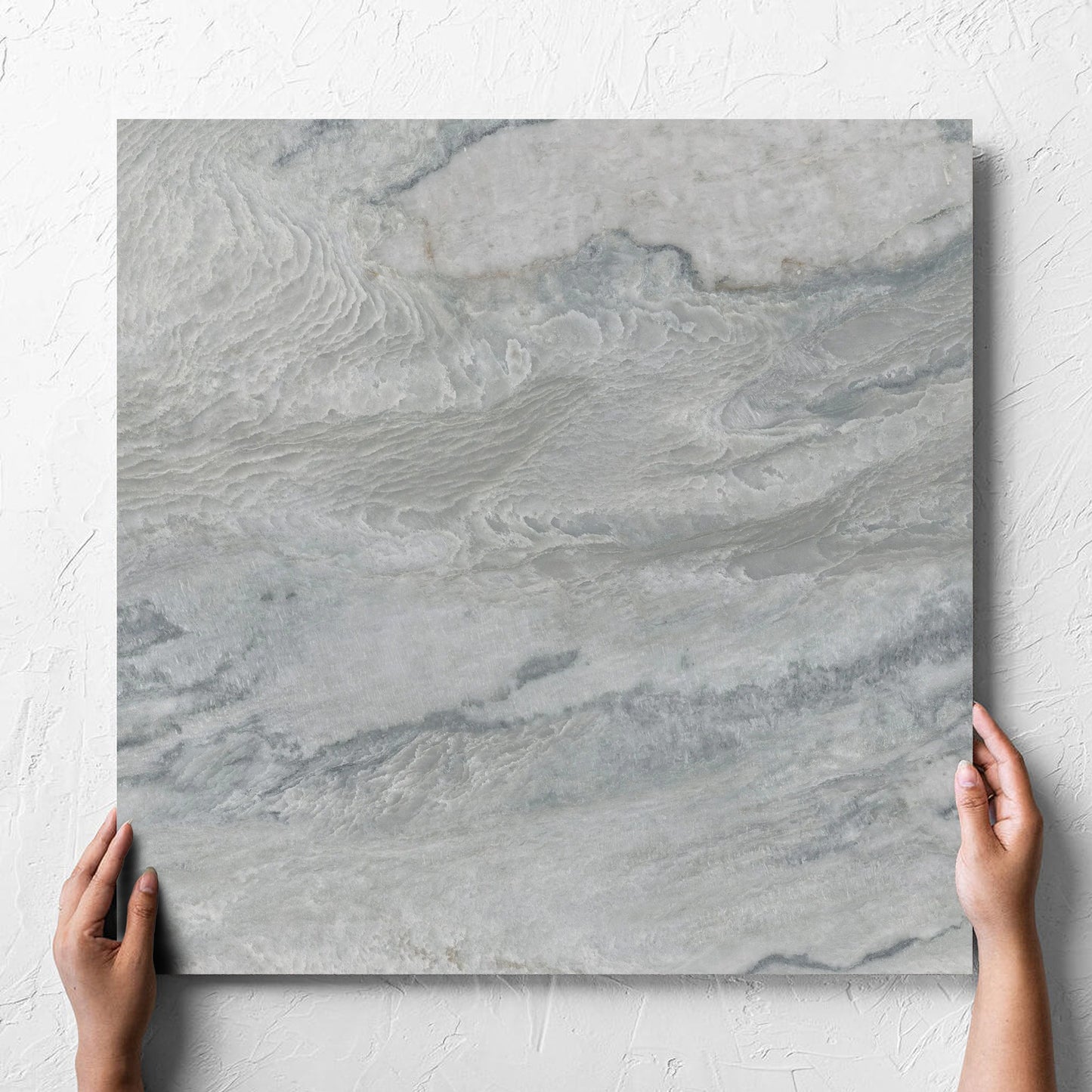 Hand holding a single Onyx Grey Polished 600x600mm tile against a white rendered wall, showing the matt surface