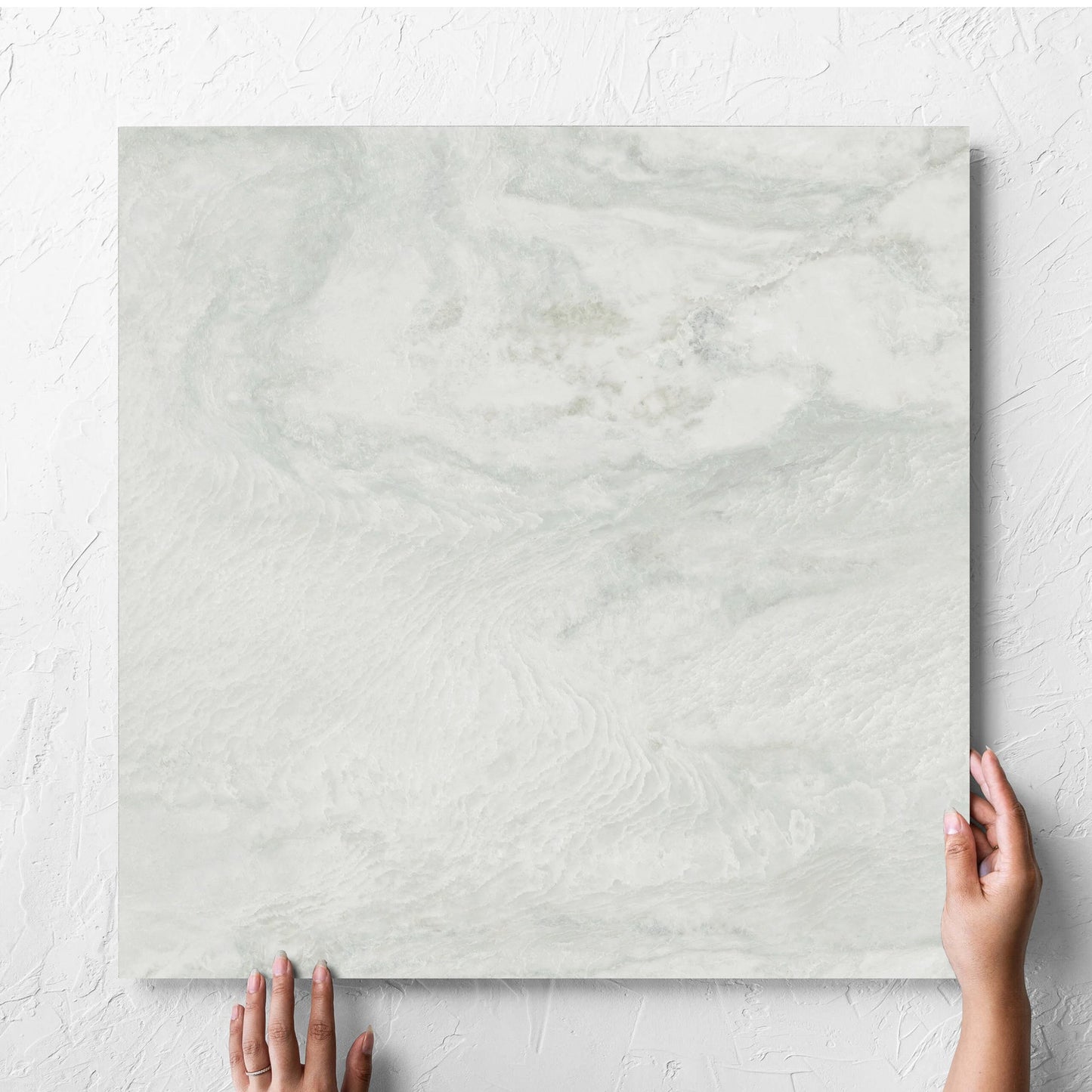 Hand holding a single Onyx White Polished 600x600mm tile against a white rendered wall, showing the matt surface