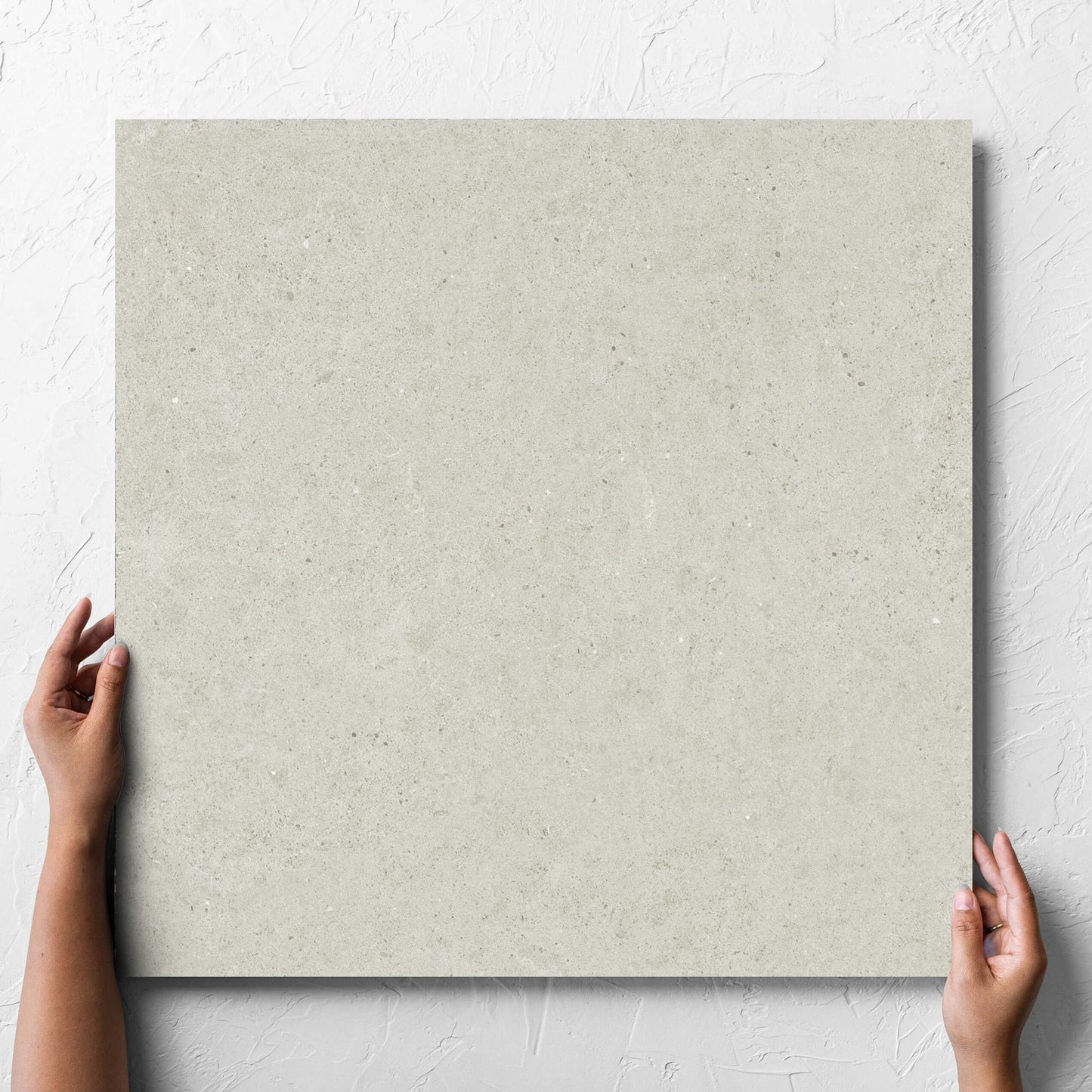 Hand holding a single Organic Pietra Lavica Birch 600x600mm tile against a white rendered wall, showing the tile surface