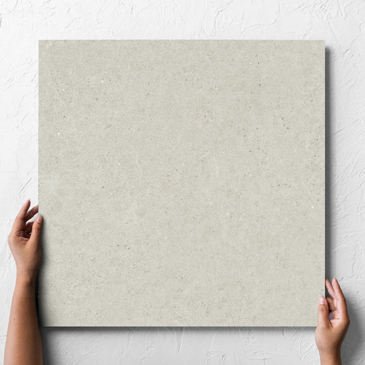 Hand holding a single Organic Pietra Lavica Birch 600x600mm tile against a white rendered wall, showing the tile surface