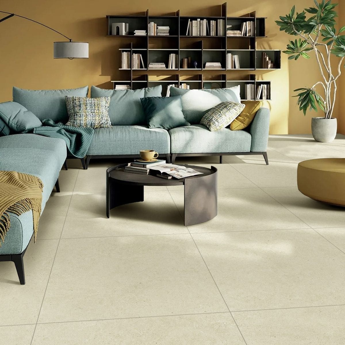 Organic Pietra Lavica Birch 600x600mm large-format cream stone-effect floor tiles in a modern living room with teal sectional sofa and dark shelving unit.