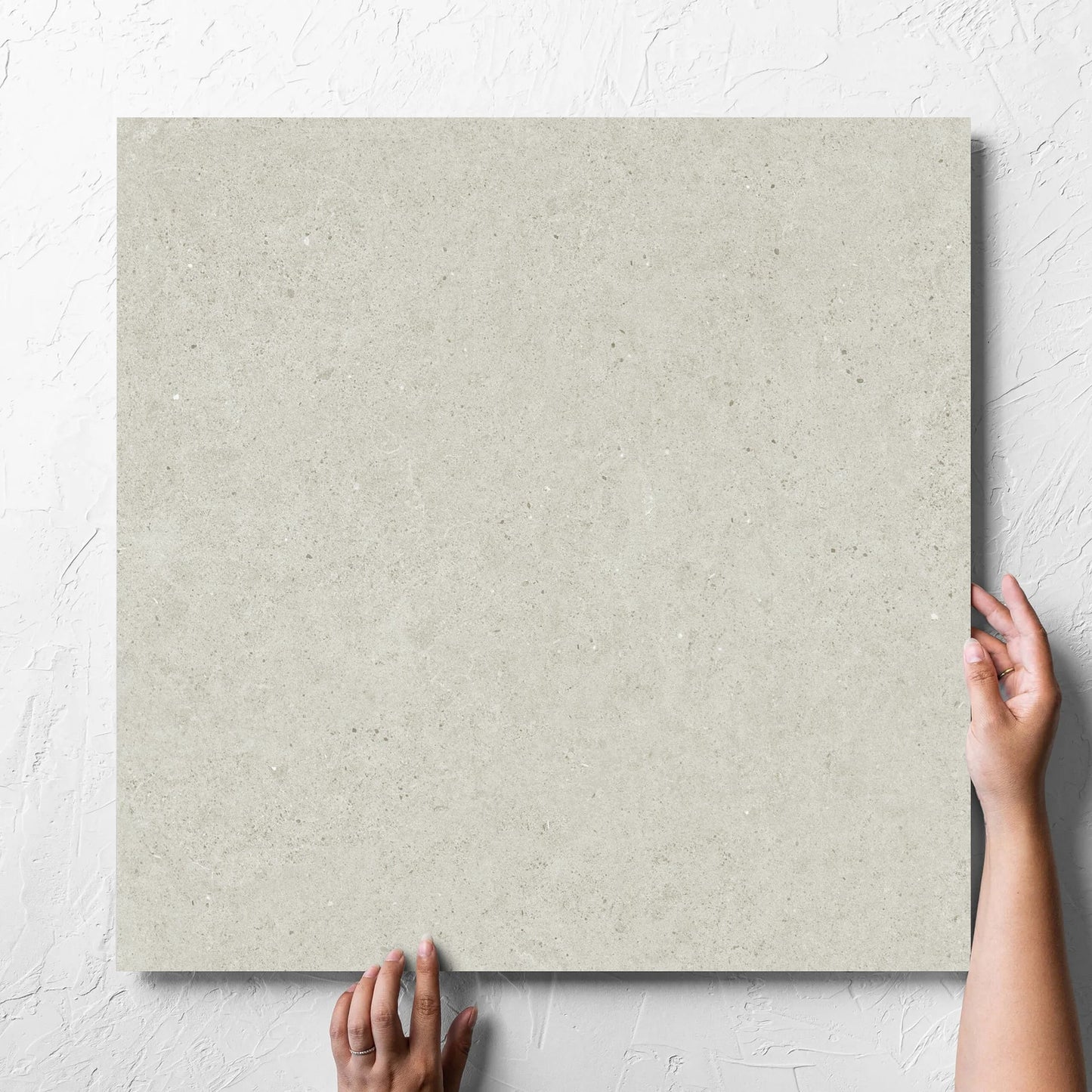 Hand holding a single Organic Pietra Lavica Birch Lappato 600x600mm tile against a white rendered wall, showing the tile surface