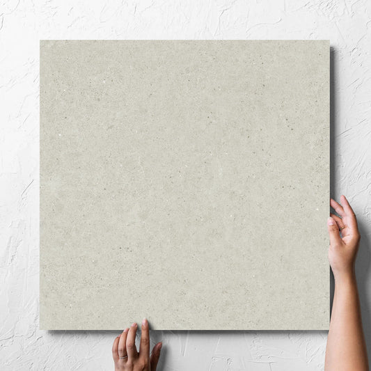 Hand holding a single Organic Pietra Lavica Birch Lappato 600x600mm tile against a white rendered wall, showing the tile surface
