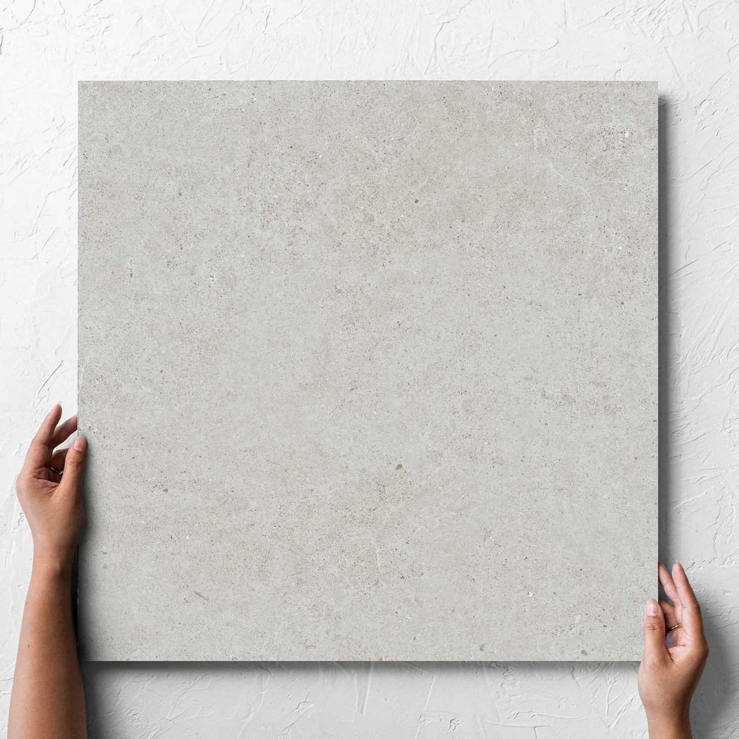 Hand holding a single Organic Pietra Lavica Glacier Lappato 600x600mm tile against a white rendered wall, showing the tile surface