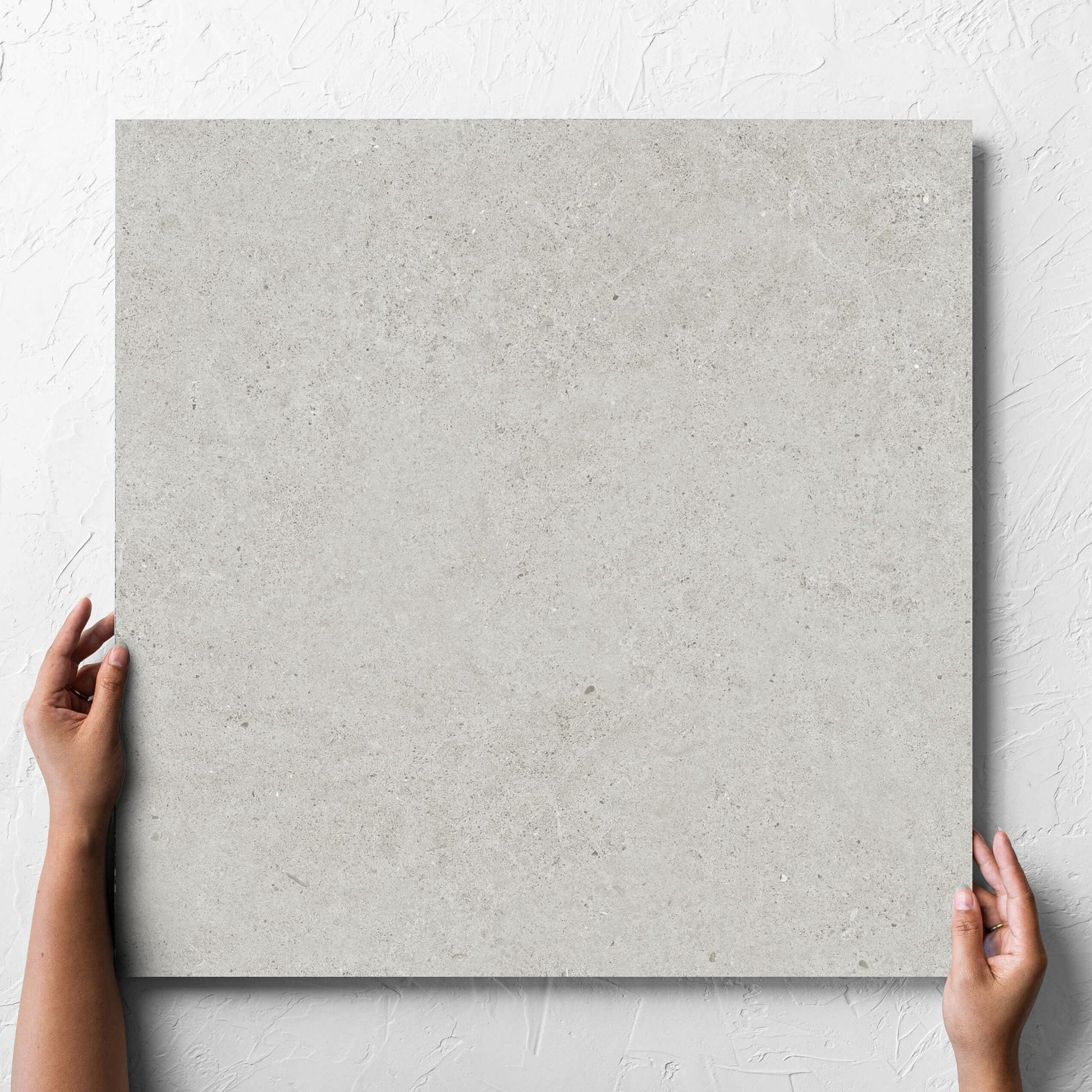 Hand holding a single Organic Pietra Lavica Glacier Lappato 600x600mm tile against a white rendered wall, showing the tile surface