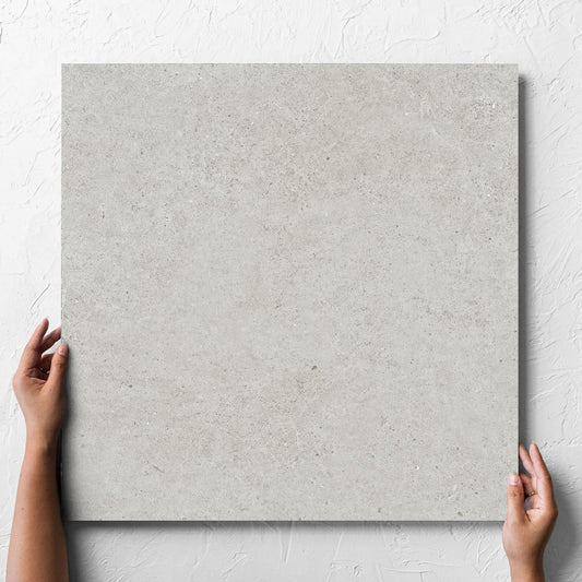 Hand holding a single Organic Pietra Lavica Glacier Lappato 600x600mm tile against a white rendered wall, showing the tile surface