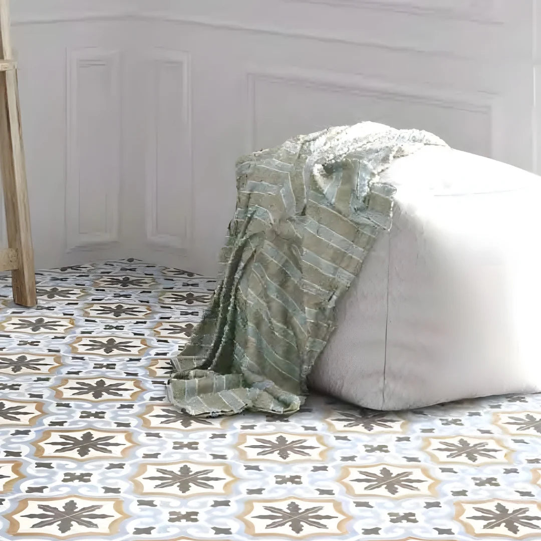 Paint Romantico Decor 205x205mm encaustic-style patterned floor tiles in grey, gold and white beneath a linen floor pouf with a draped sage throw.