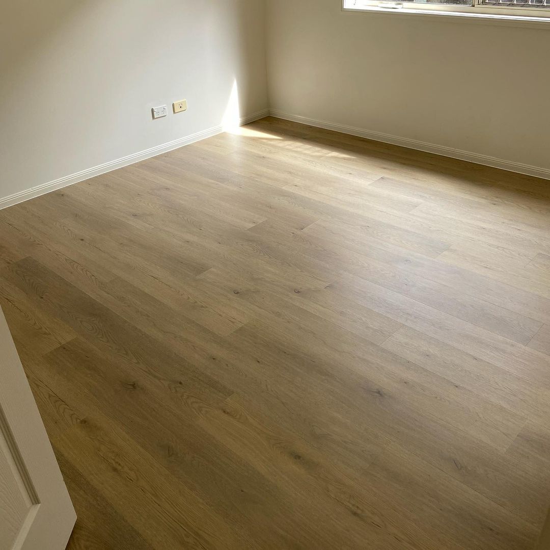 Pale Sand Elegant SPC Hybrid 6.5mm Flooring 5+1.5mm installed in a bright empty bedroom with white walls, white skirting boards, and natural light from a window.