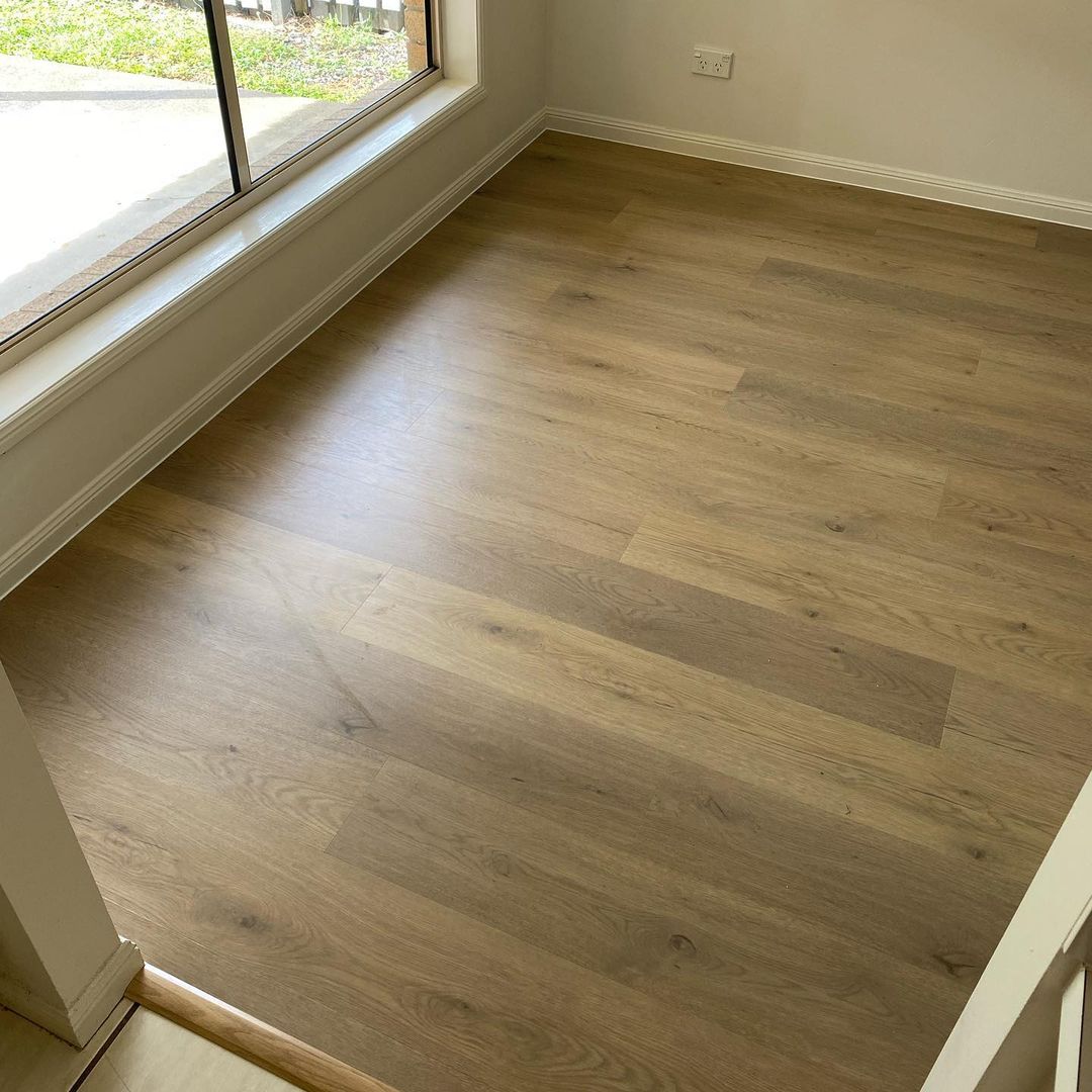 Pale Sand Elegant SPC Hybrid 6.5mm Flooring 5+1.5mm installed in a bright empty room with large windows and white skirting boards.