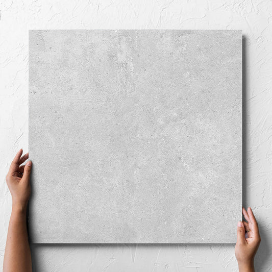 Hand holding a single Paradigm Light Grey Structured Paver 600x600x20mm tile against a white rendered wall, showing the tile surface