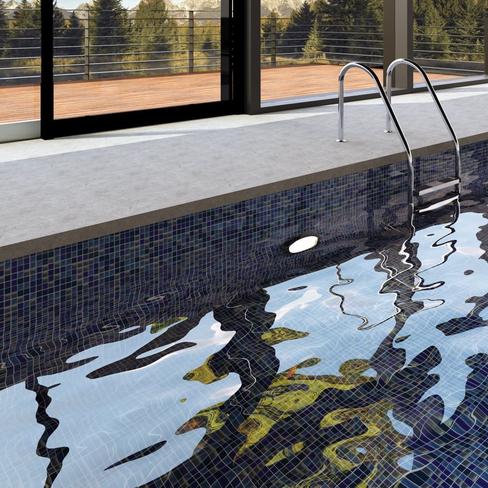 Paradise Bali Glass Mosaic Pool Safe 300x300mm tiles lining an indoor swimming pool with chrome ladder, dark iridescent finish reflecting mountain views through floor-to-ceiling windows.