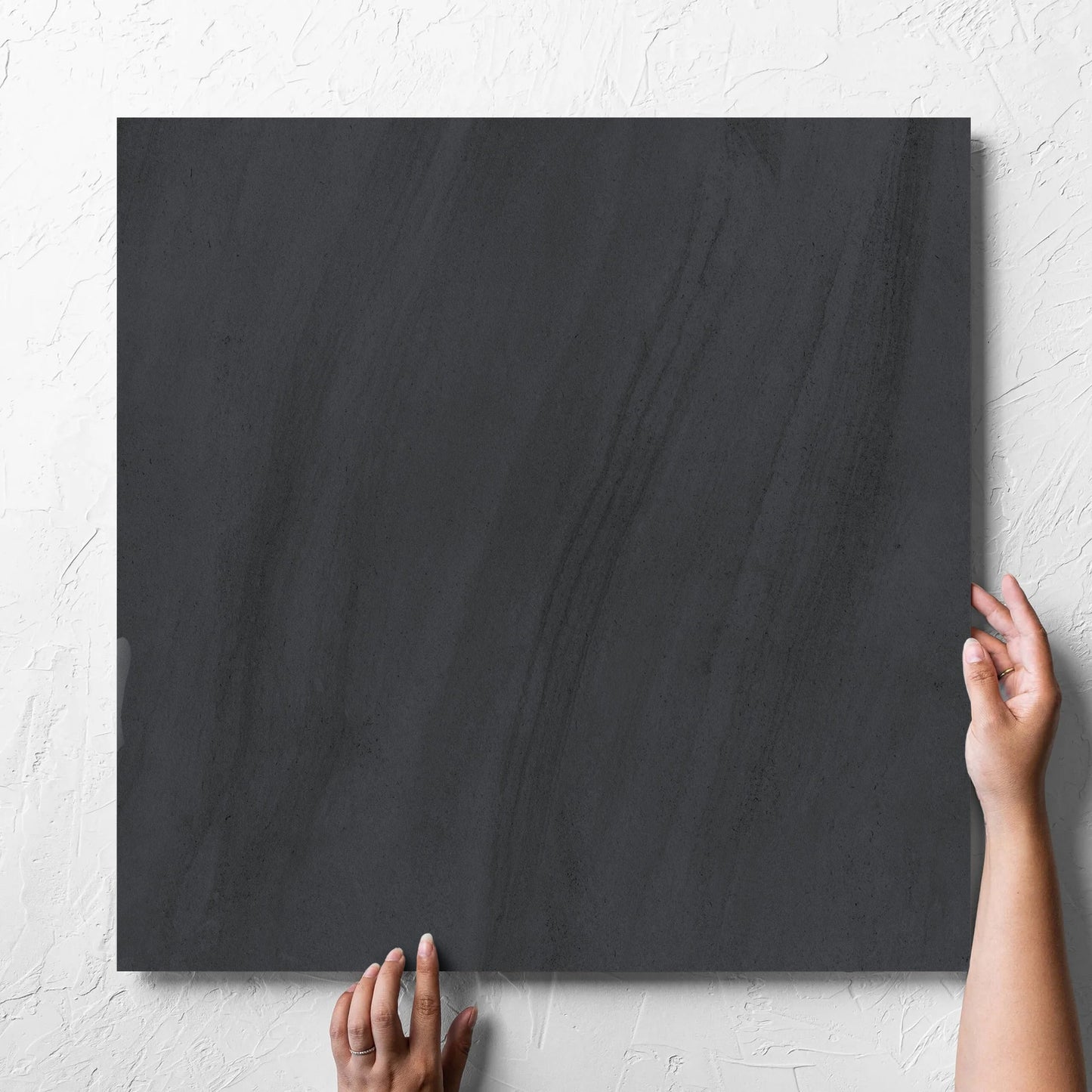 Hand holding a single Paris Noir Matt 600x600mm tile against a white rendered wall, showing the matt surface