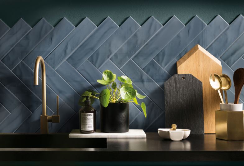 Pasha Dark Blue Gloss 75x300mm tiles installed as a herringbone kitchen splashback, styled with brass tapware, wooden chopping boards, and a green potted plant.
