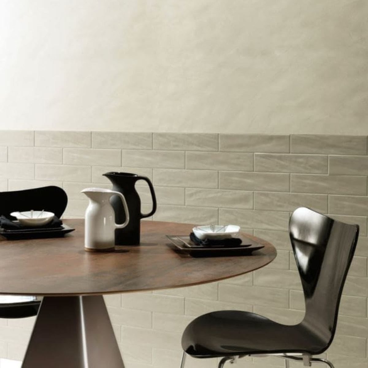 Pasha Desert Gloss 75x300mm cream gloss subway tiles installed as a half-wall dado in a modern dining room with a round walnut table and black chairs.
