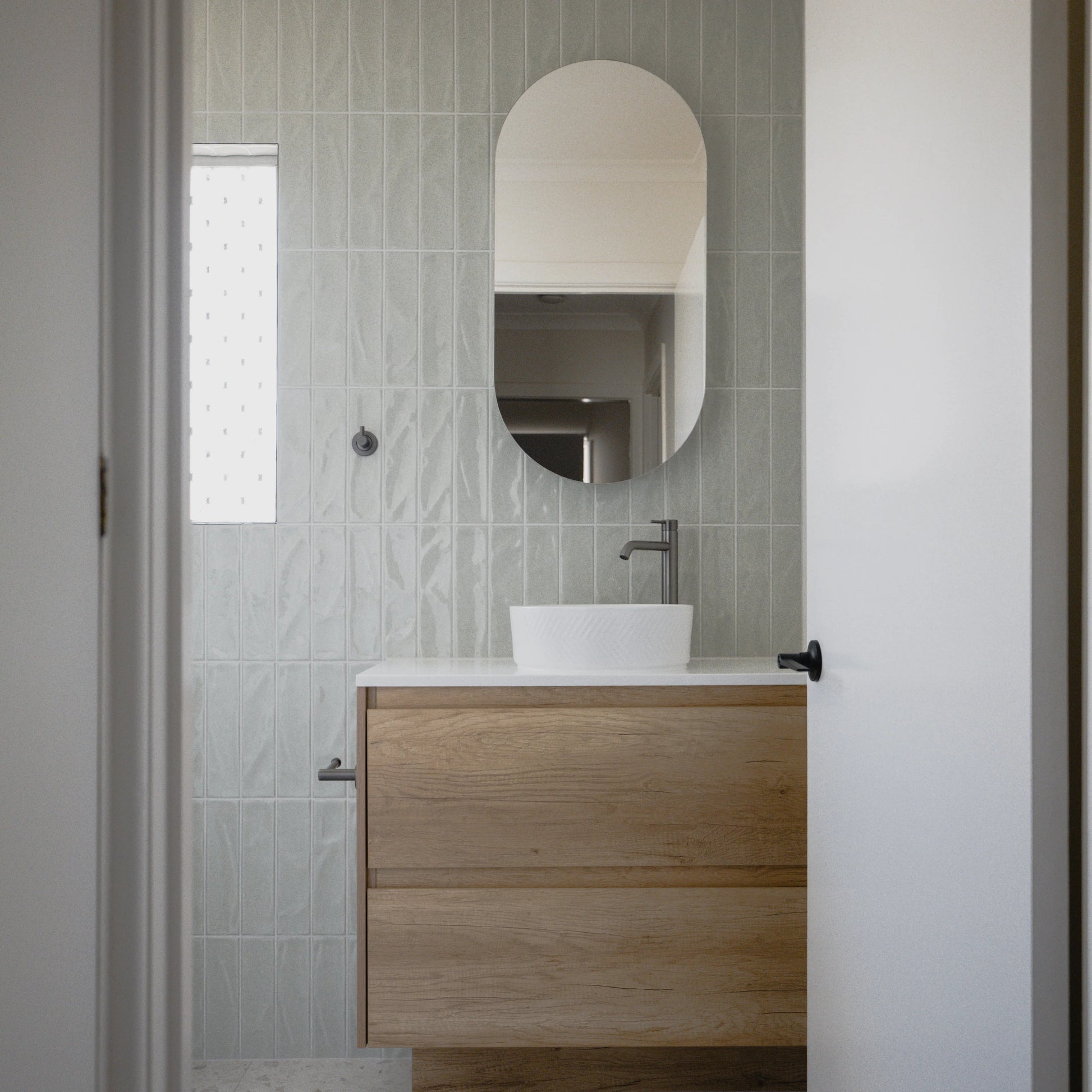 Pasha Sage Gloss 75x300mm tiles cover a full-height bathroom wall behind a floating timber vanity with a white vessel sink and oval mirror.