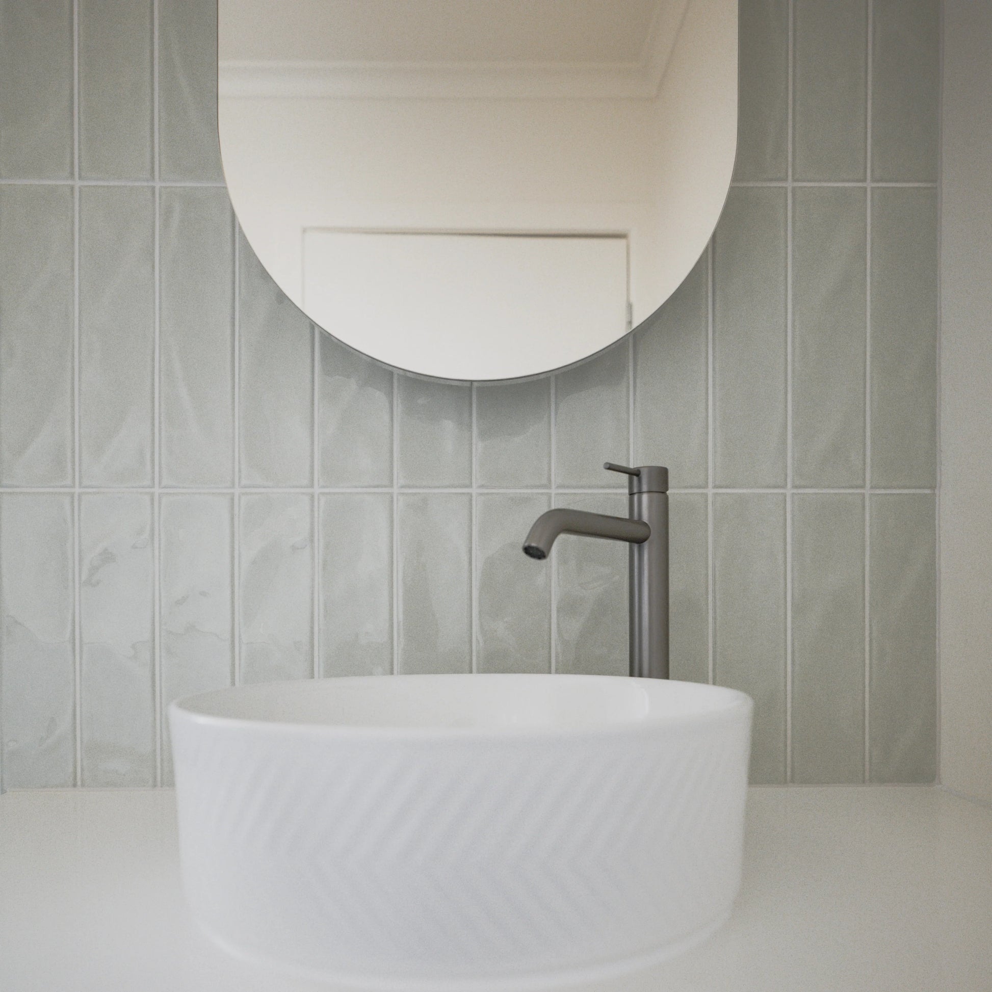 Pasha Sage Gloss 75x300mm wall tiles installed as a vertical stack-bond bathroom splashback behind a white vessel basin and matte gunmetal tap.