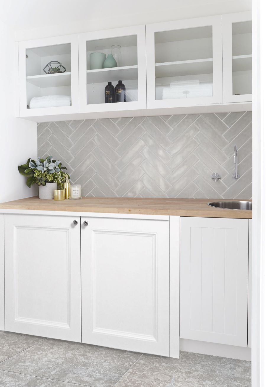 Pasha Smoke Gloss 75x300mm tiles laid in a herringbone pattern as a laundry splashback, paired with white shaker cabinets and a timber benchtop.