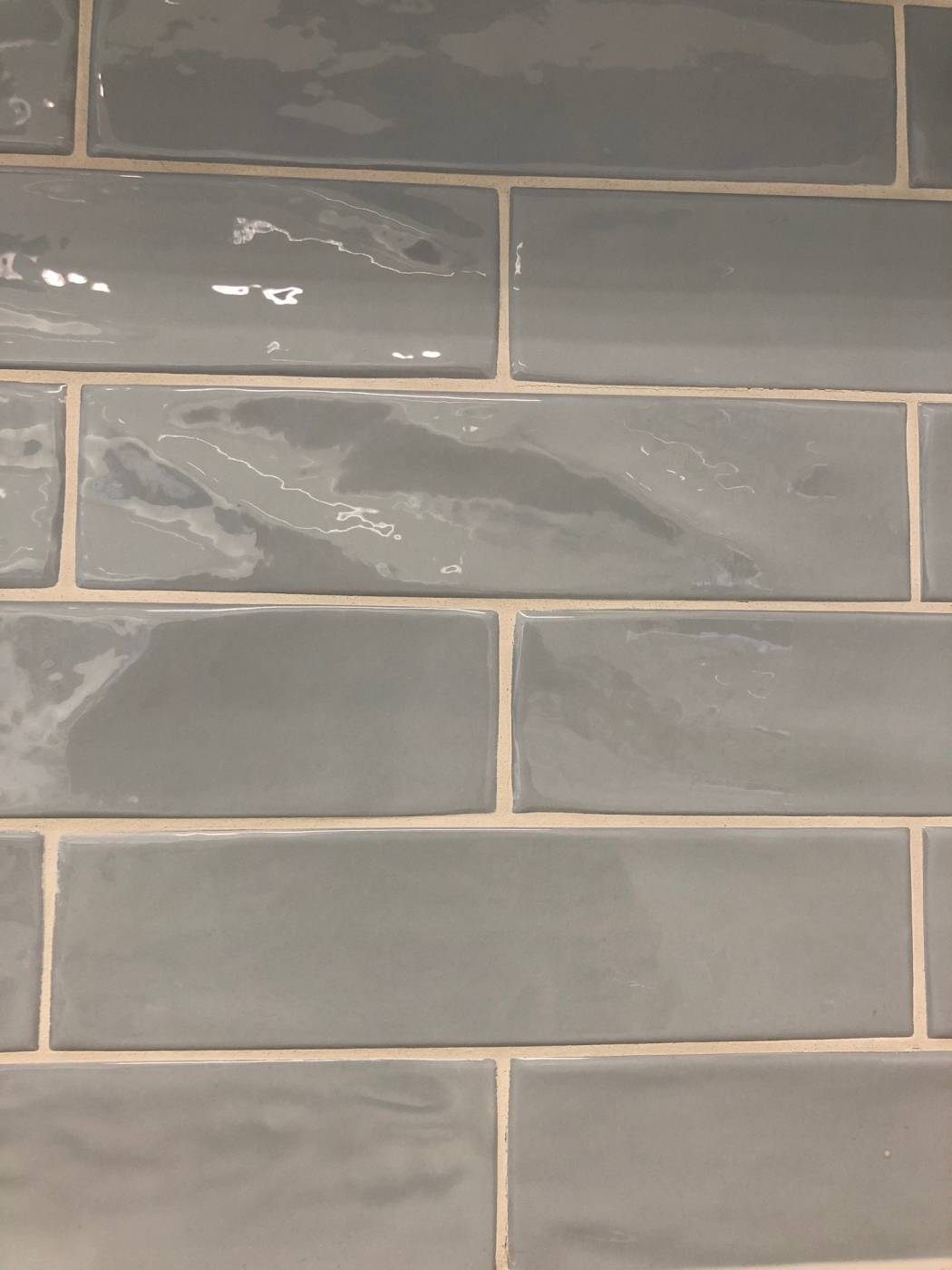 Close-up of Pasha Steel Blue Gloss 75x300mm subway tiles in a staggered brick pattern with sandy grout and a reflective glazed finish.