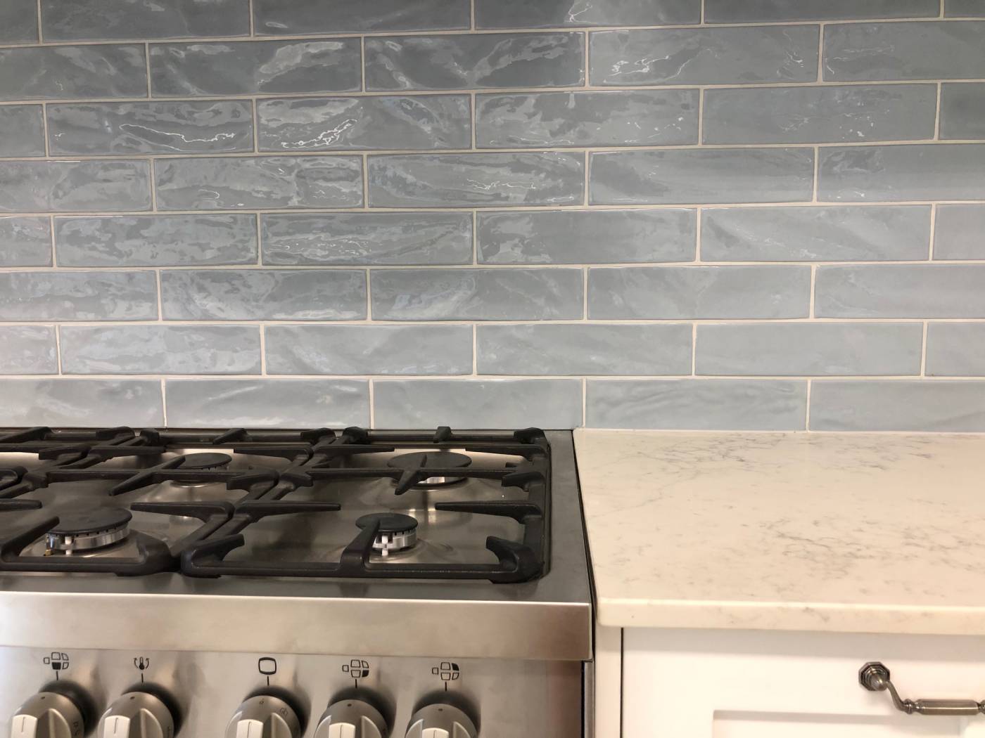Pasha Steel Blue Gloss 75x300mm tiles installed as a kitchen splashback behind a stainless steel gas range with marble countertop.