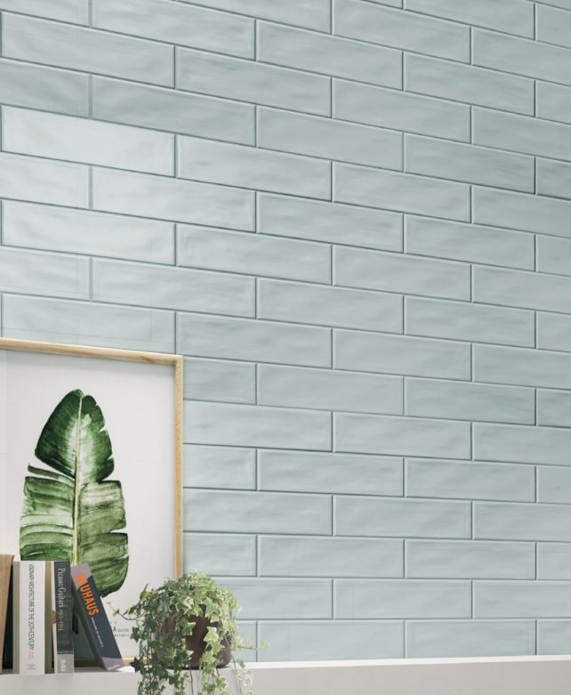 Pasha Steel Blue Gloss 75x300mm tiles installed as a full wall in a soft sage green finish, styled with botanical art print and trailing ivy plant.