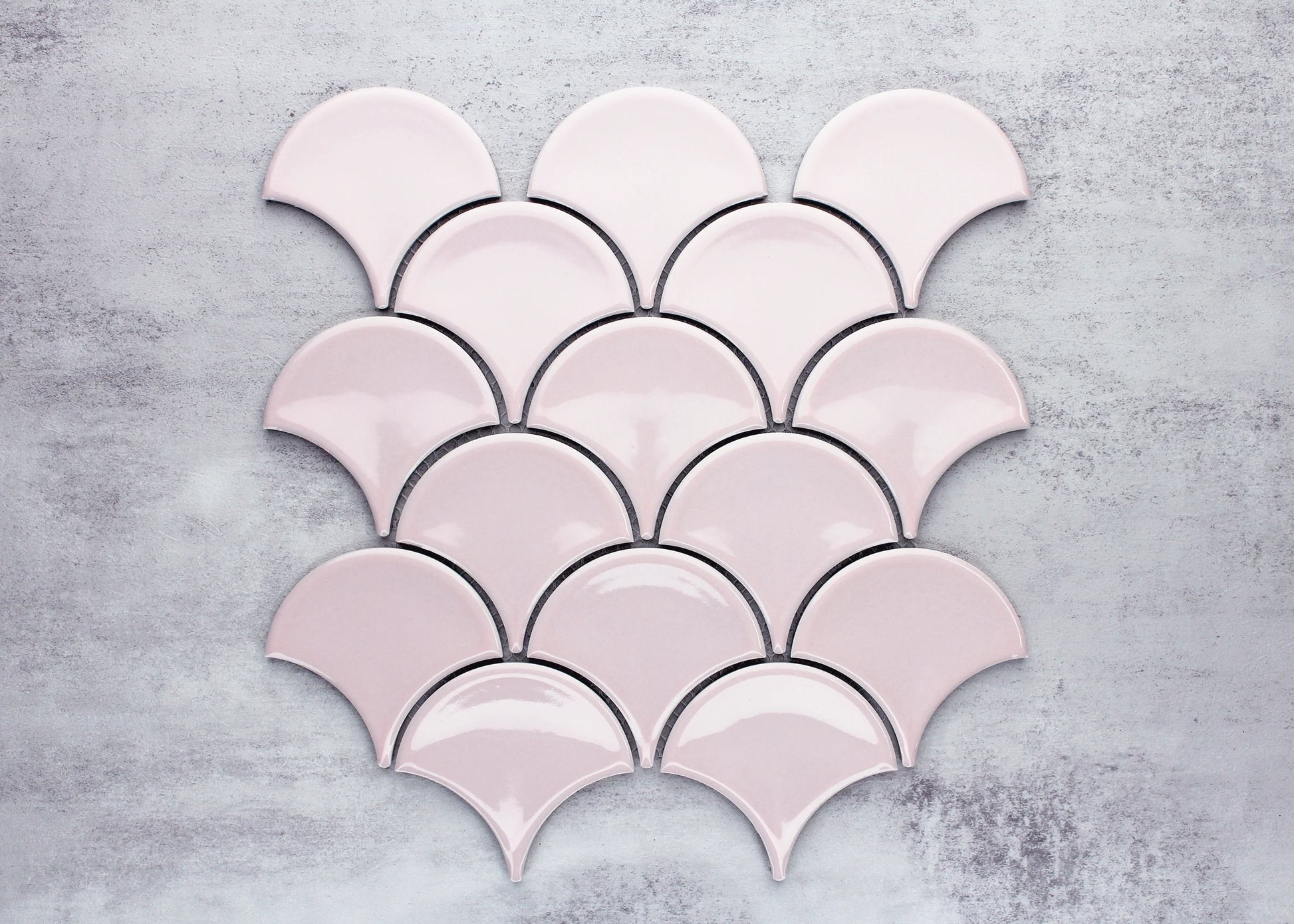 Pastel Pink Gloss Glazed Porcelain Fishscale 95x87mm tiles arranged in an overlapping scallop pattern, showcasing their fan-shaped form and glossy pink glaze against a grey concrete background.