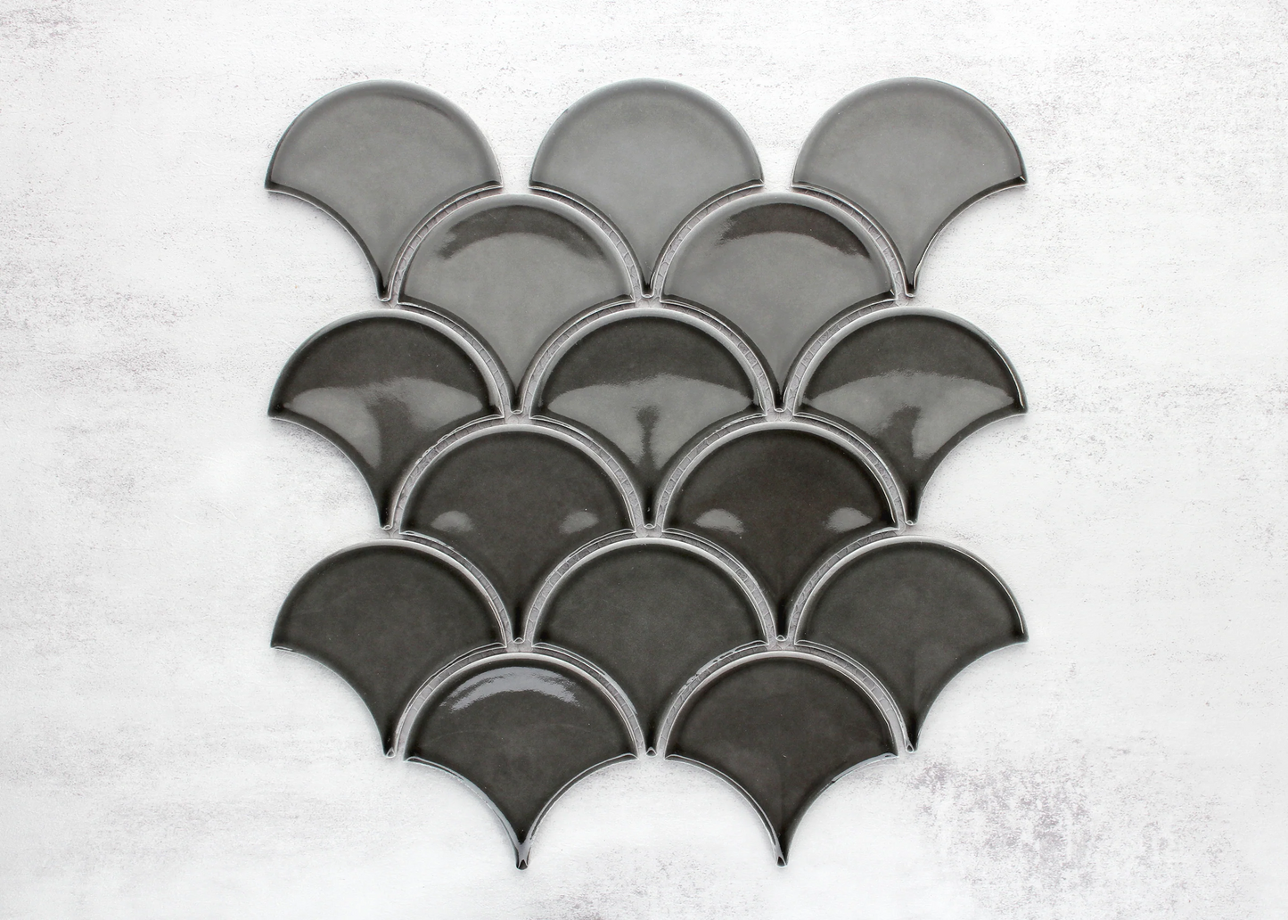 Pack shot of PGFS-8874 Charcoal Gloss Glazed Porcelain Fishscale 95x87mm tiles arranged in an overlapping scallop pattern showing deep charcoal glaze and fan-shaped profile.