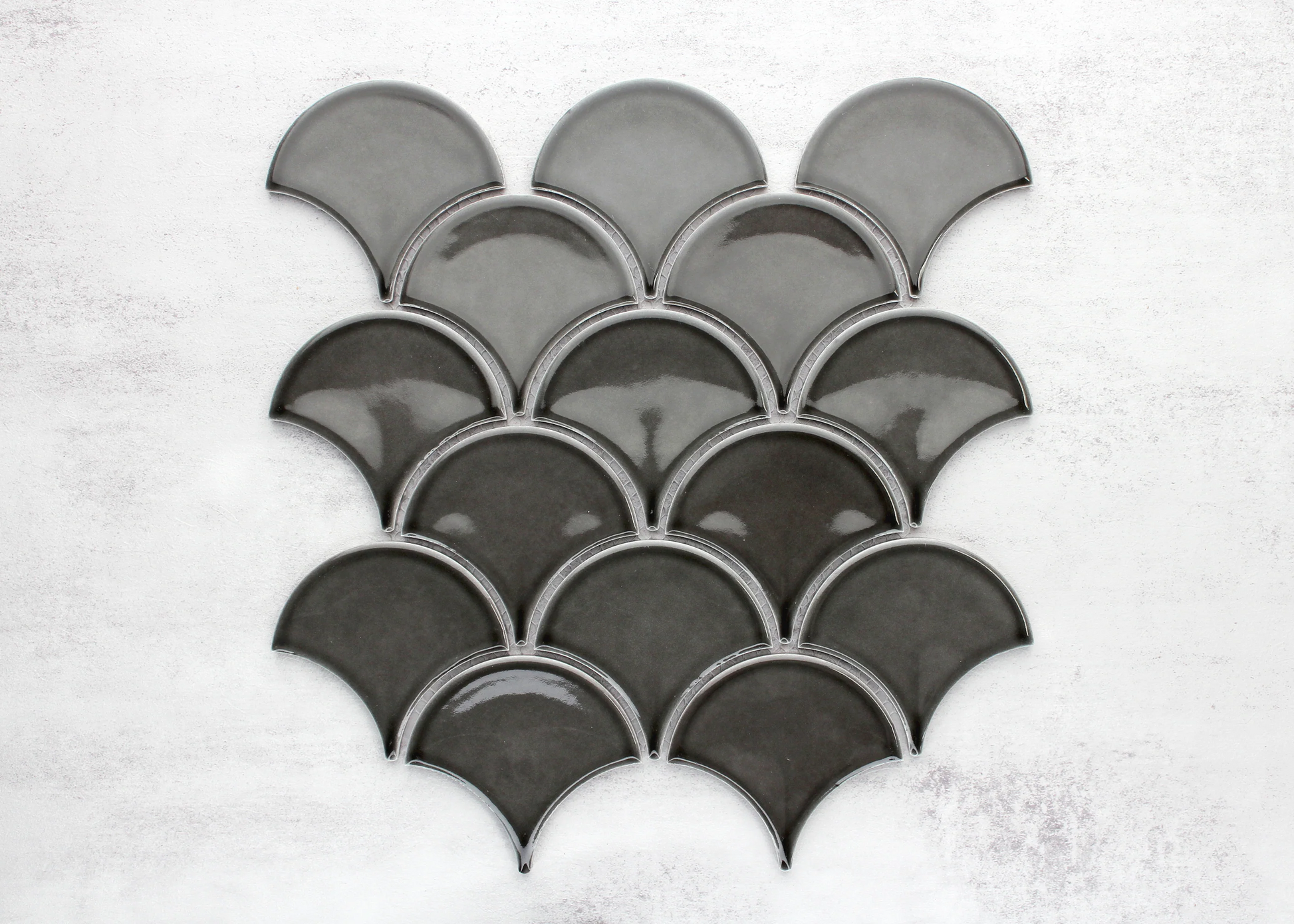 Pack shot of PGFS-8874 Charcoal Gloss Glazed Porcelain Fishscale 95x87mm tiles arranged in an overlapping scallop pattern showing deep charcoal glaze and fan-shaped profile.