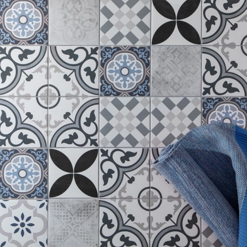 Picasso Fleur 200x200mm encaustic-style patchwork floor tiles in blue, grey and white with a folded blue towel resting on top.