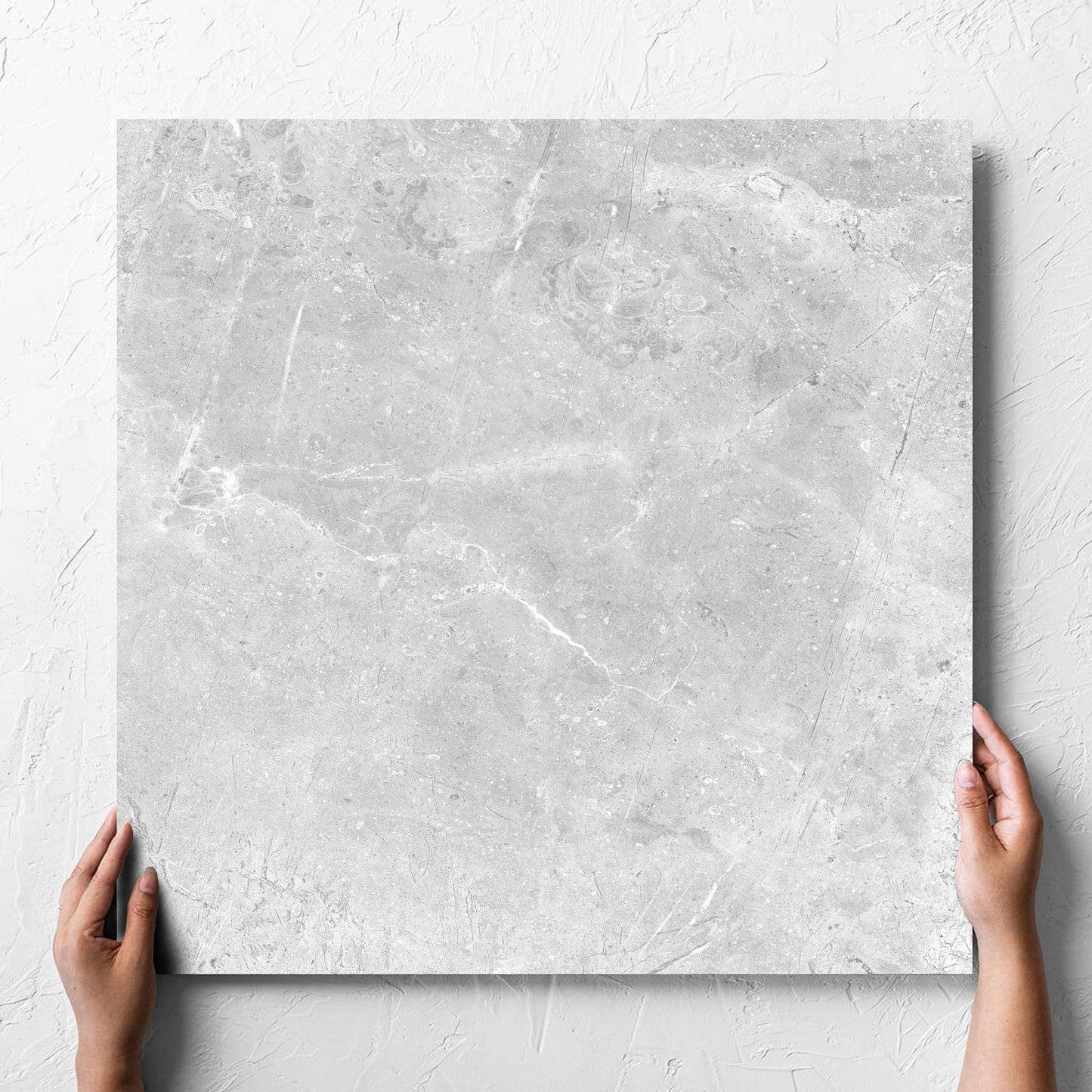 Hand holding a single Potifino Oyster Matt 600x600mm tile against a white rendered wall, showing the matt surface
