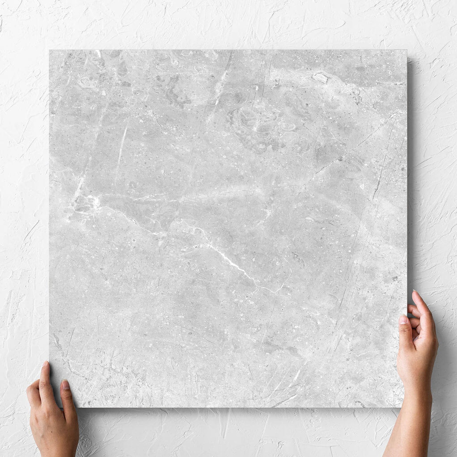 Hand holding a single Potifino Oyster Polished 600x600mm tile against a white rendered wall, showing the matt surface