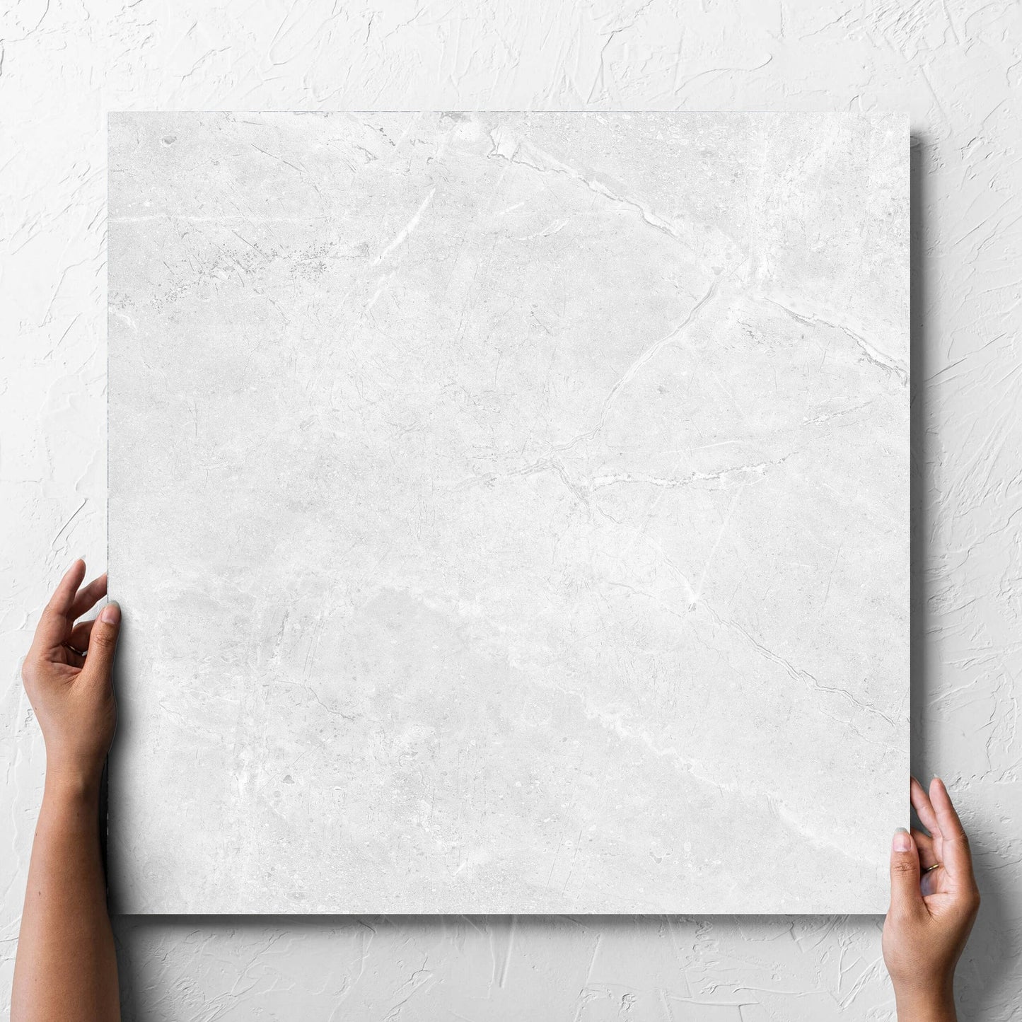 Hand holding a single Potifino White Matt 600x600mm tile against a white rendered wall, showing the matt surface