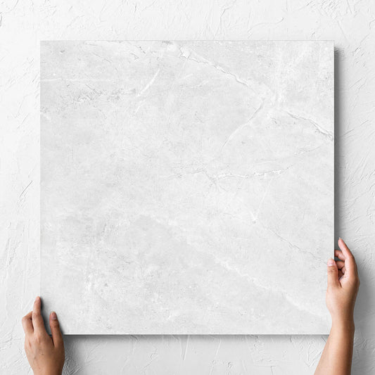 Hand holding a single Potifino White Polished 600x600mm tile against a white rendered wall, showing the matt surface