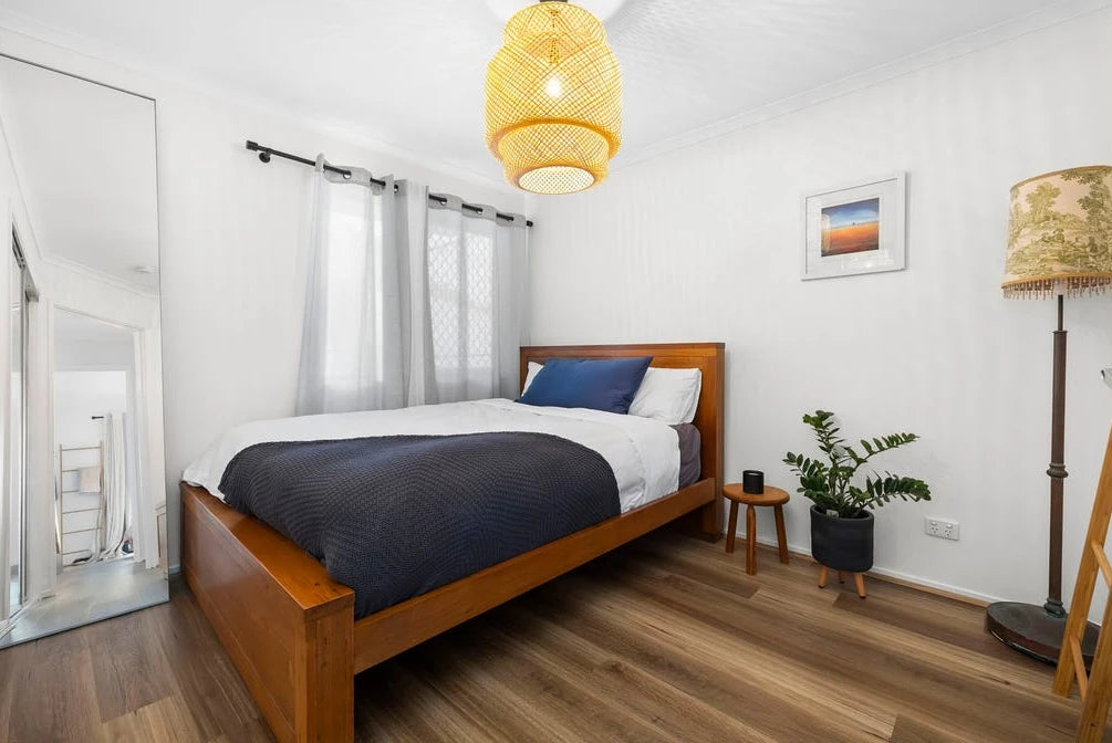 Queensland Spotted Gum Elegant SPC Hybrid 6.5mm Flooring 5+1.5mm installed in a bright bedroom with a timber bed frame, woven pendant light, and indoor plant.