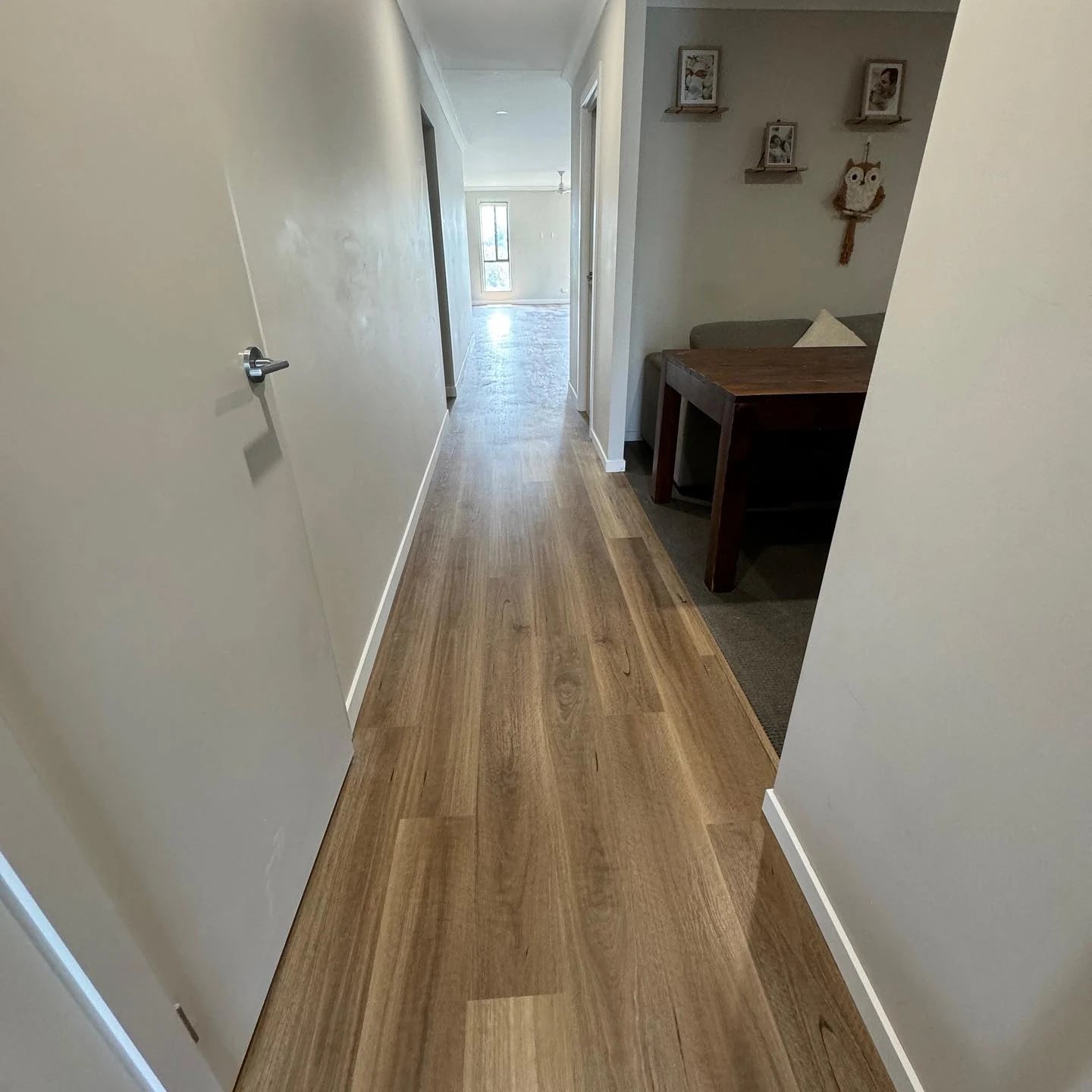 Queensland Spotted Gum Elegant SPC Hybrid 6.5mm Flooring 5+1.5mm installed in a bright residential hallway with white walls, leading to a sunlit living area with a timber dining table visible.
