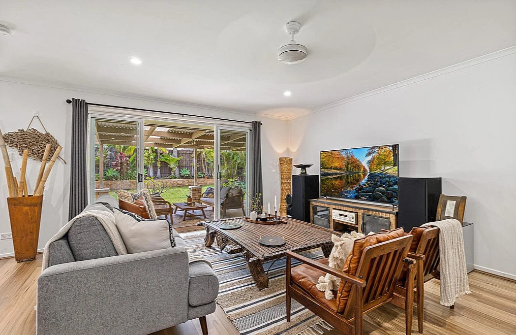 Queensland Spotted Gum Elegant SPC Hybrid 6.5mm Flooring 5+1.5mm installed in a bright living room with grey sofa, timber coffee table, and sliding doors opening to a lush outdoor patio.