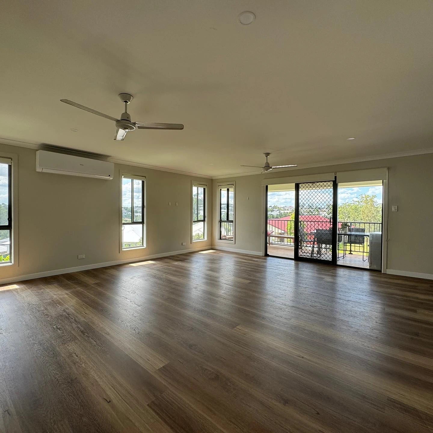 Queensland Spotted Gum Elegant SPC Hybrid 6.5mm Flooring 5+1.5mm installed in a spacious open-plan living room with ceiling fans, split-system air conditioning, and sliding doors opening to a sunny balcony.