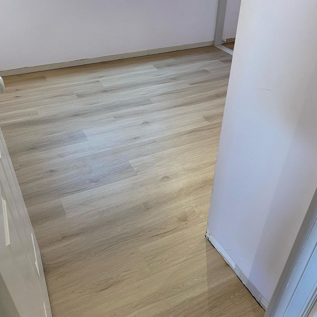 Raw Neutral Elegant SPC Hybrid 6.5mm Flooring 5+1.5mm installed in an empty hallway, showcasing light beige wood-look planks with subtle grey undertones against white walls.