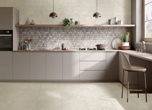 Riviera Ivory 600x600mm tiles used on a modern kitchen floor and walls, complementing taupe cabinetry, a patterned splashback, and copper pendant lights.