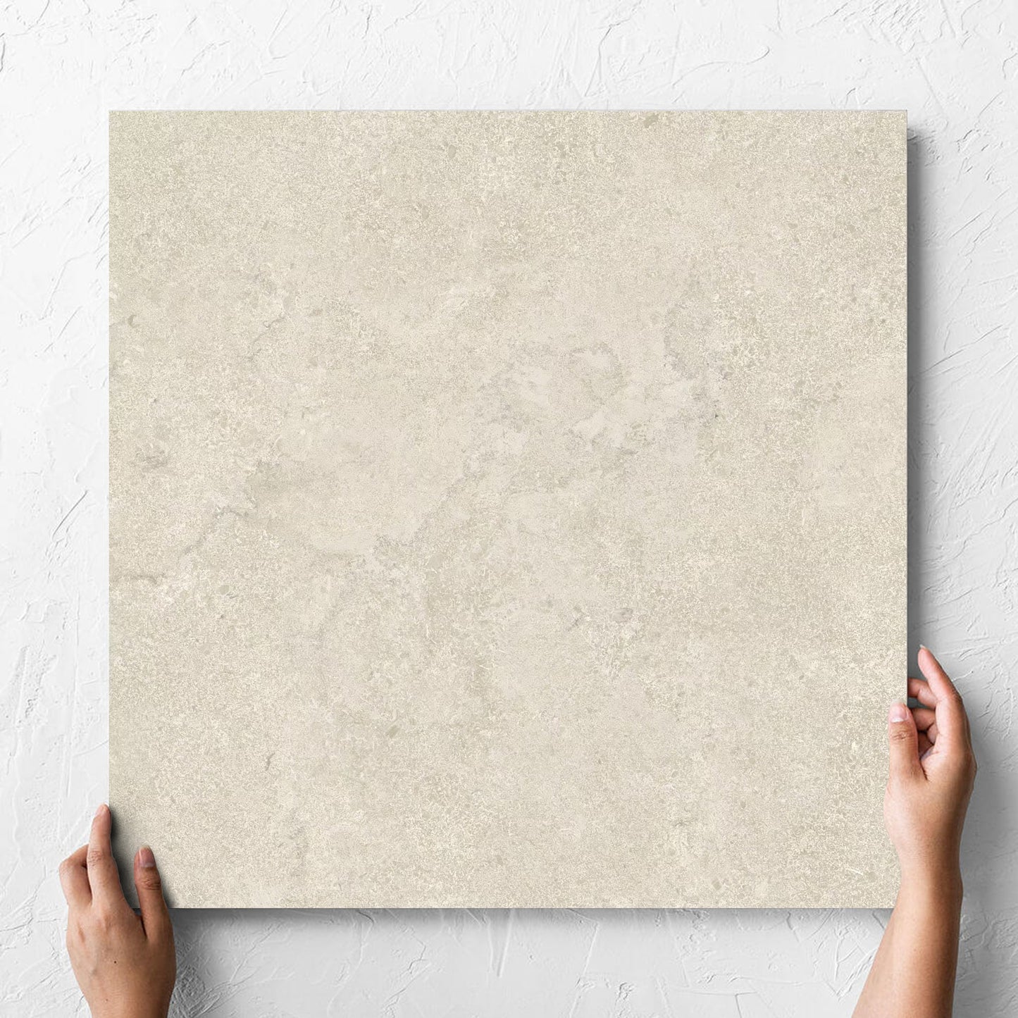 Hand holding a single Roman Travertine Beige 600x600mm tile against a white rendered wall, showing the beige matt surface